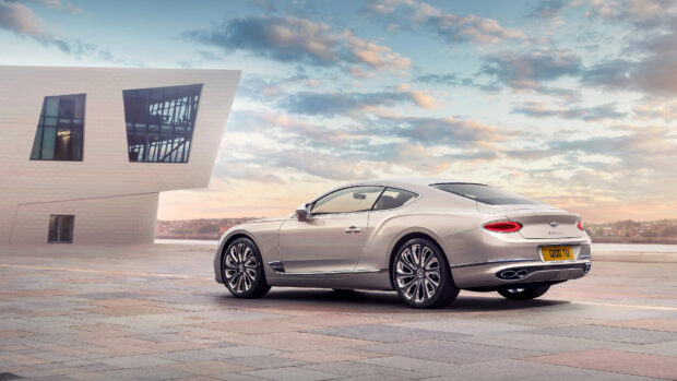 A sleek Bentley Continental car parked near a modern building under a cloudy sky