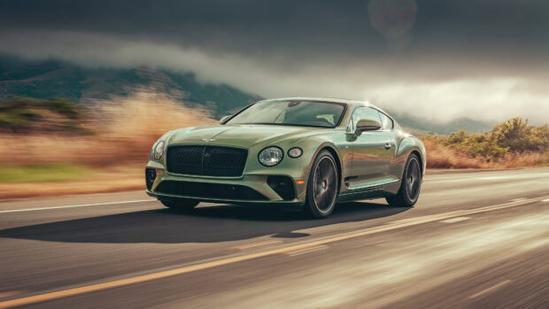 A green Bentley Continental driving fast on a scenic road with hills in the background