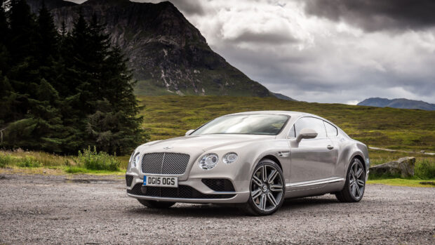 A sleek Bentley Continental parked on a gravel road with mountains and trees in the background