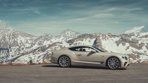 Beige Bentley Continental car parked on mountain road with snowy peaks in background