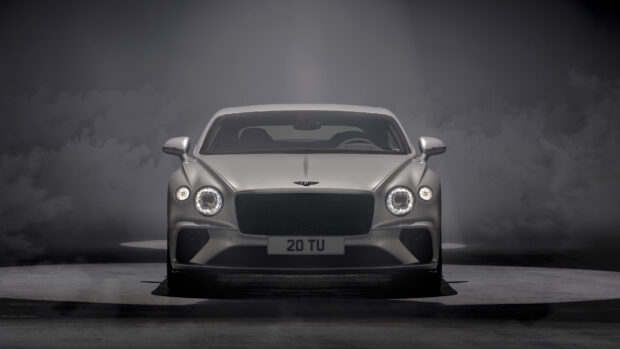 Front view of a Bentley Continental car with bright headlights on a dark background