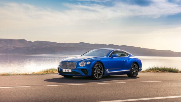 Blue Bentley Continental car parked on road near lake and mountains
