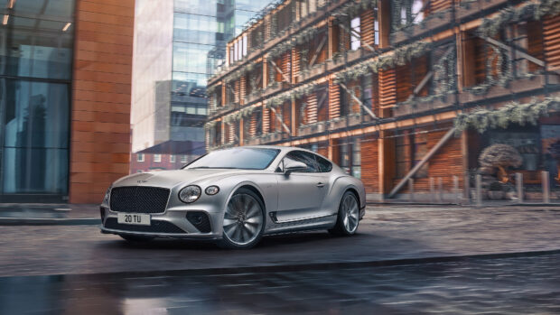 Silver Bentley Continental driving fast in urban area with modern buildings in background