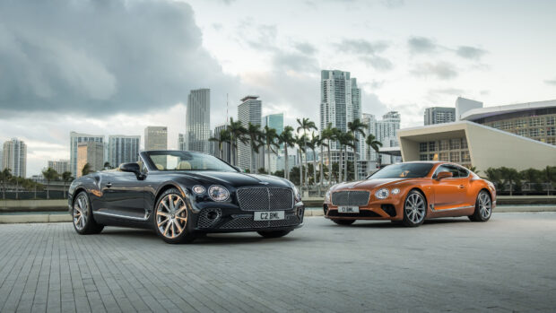 Two Bentley Continental cars parked in front of a city skyline with palm trees under cloudy sky