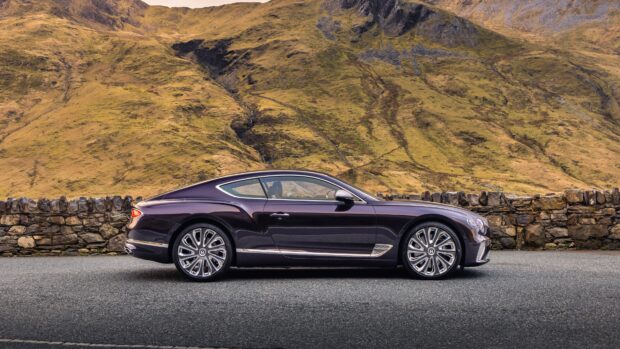 A Bentley Continental car parked on a road near a stone wall and autumn hills