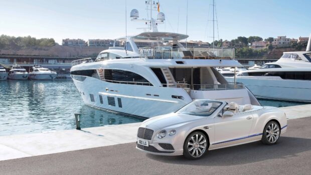 A Bentley Continental convertible parked near a luxury yacht at the marina