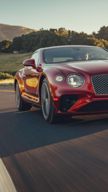 Red Bentley Continental driving on a scenic road with green hills in the background