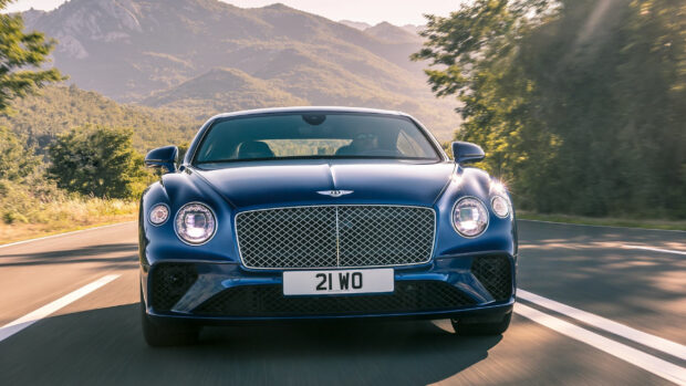 Blue Bentley car driving on a mountain road with sunlight and trees around