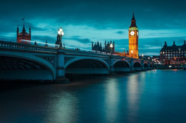 Illuminated Big Ben tower visible from the bridge over the river at twilight