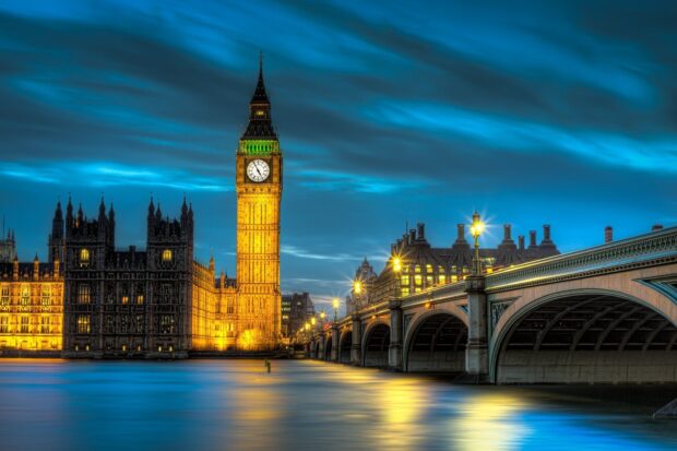 Illuminated Big Ben Tower with surrounding architecture over calm river in London at dusk