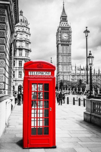 Red telephone booth near Big Ben in London cityscape with cloudy sky