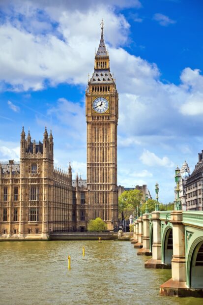 Big Ben tower stands tall by the river under a bright blue sky