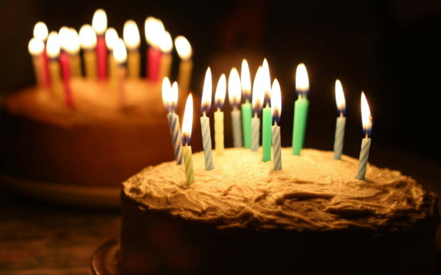 A birthday party cake with lit candles glowing warmly in a dark room
