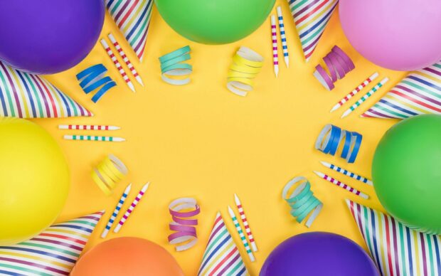 Colorful party decorations with balloons party hats and candles on a yellow surface for birthday celebration