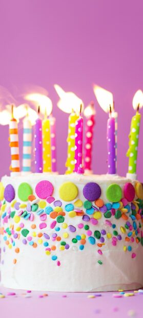 Colorful birthday party cake with candles and confetti decorations on a pink background
