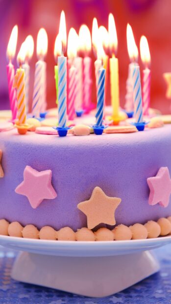 Colorful birthday party cake decorated with star shapes and striped candles burning brightly