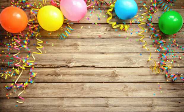 Colorful balloons and confetti decorate the wooden table for a birthday party celebration