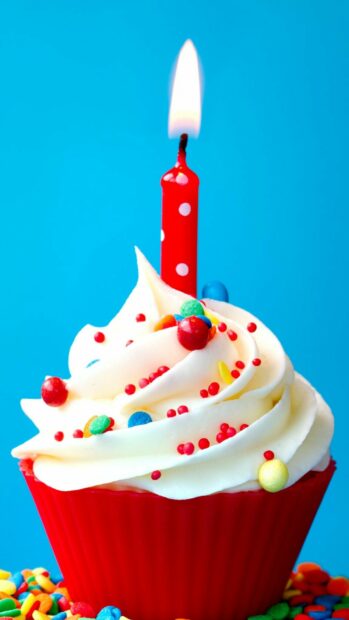 A colorful birthday party cupcake with a lit candle and festive sprinkles