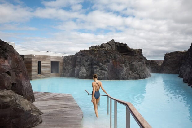 Woman in swimsuit walking into Blue Lagoon Iceland geothermal lagoon surrounded by volcanic rocks