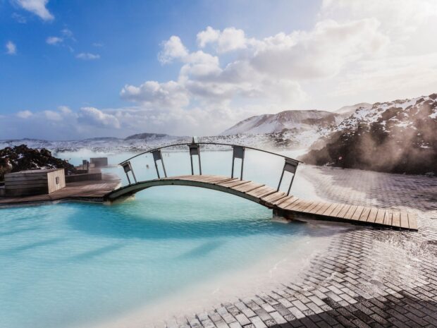 A serene view of Blue Lagoon Iceland featuring a wooden bridge over steaming blue water surrounded by snowy landscape