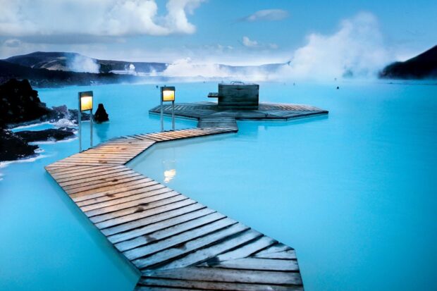 A wooden walkway over the blue lagoon in Iceland surrounded by volcanic landscape and steam