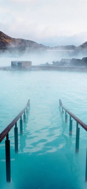 Steam rising over the blue lagoon Iceland natural geothermal spa water with metal handrails