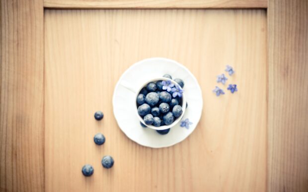 A cup filled with fresh blueberry and small purple flowers on a wooden surface