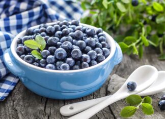 A bowl filled with fresh blueberry and green leaves on a wooden table