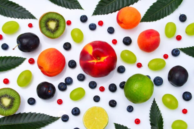 Fresh blueberries scattered among various fruits with green leaves on a white surface