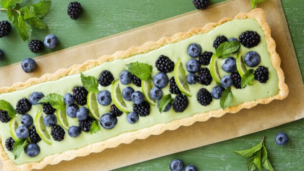 A delicious tart topped with fresh blueberry and blackberry garnished with lime slices and mint leaves