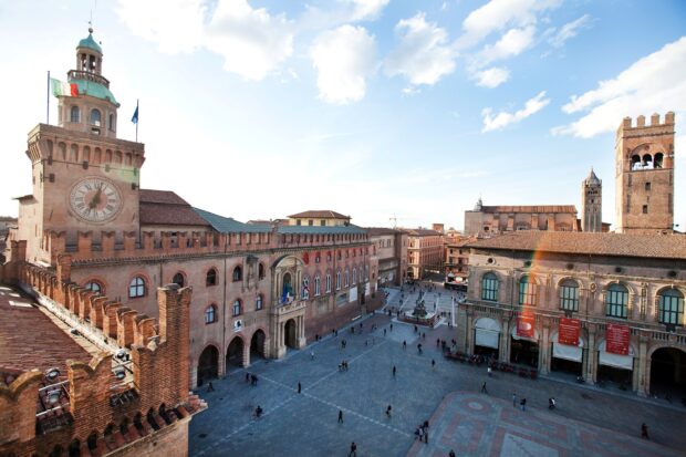 Historic Bologna city square with ancient clock tower and old buildings under clear sky