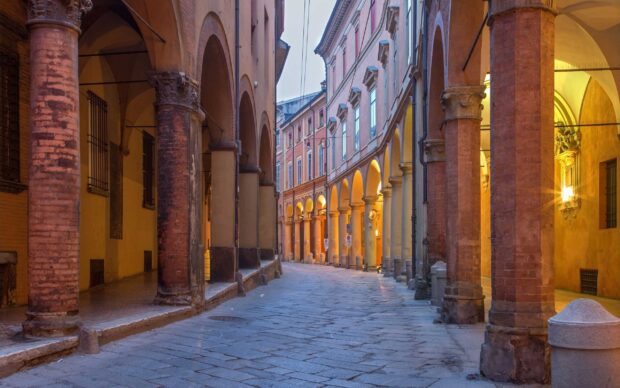 Historic Bologna street with ancient archways and columns illuminated by warm light
