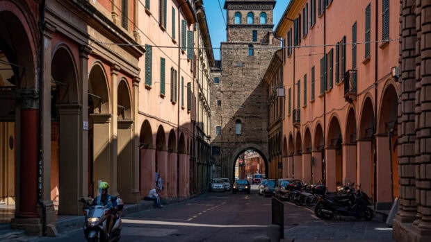 Historic street in Bologna with ancient arches and a stone tower in clear sunlight