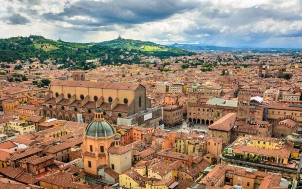 A panoramic view of Bologna cityscape with historic buildings and green hills on a cloudy day