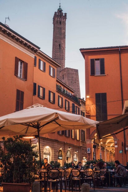 Evening street scene in Bologna with historical tower and outdoor cafe seating