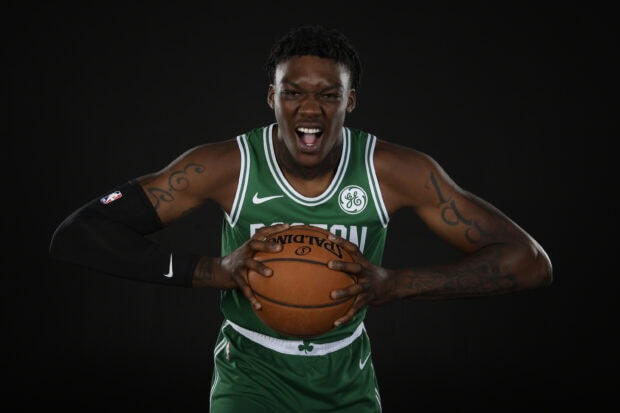 Boston Celtics player holding a basketball in green jersey with tattoos on arms
