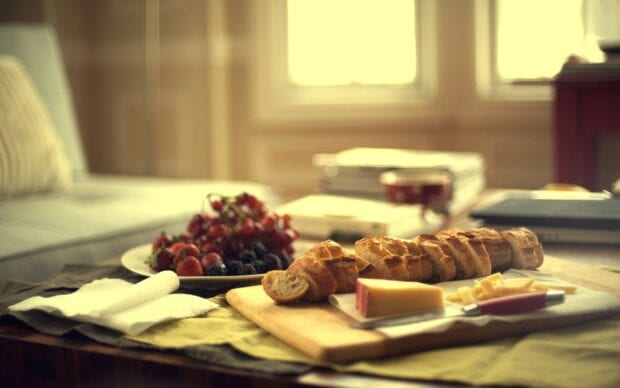 A fresh sliced bread with cheese on a wooden board near a plate of fresh berries