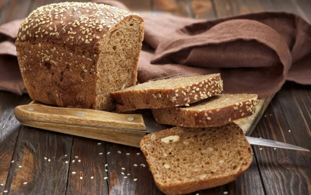 Whole wheat bread loaf with sesame seeds and slices on a wooden cutting board