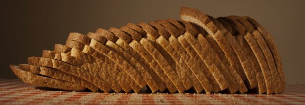 A loaf of bread neatly sliced on a tiled surface with crumbs scattered around
