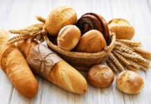 A basket of assorted fresh bread loaves and wheat stalks on a wooden surface