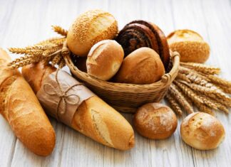 A basket of assorted fresh bread loaves and wheat stalks on a wooden surface