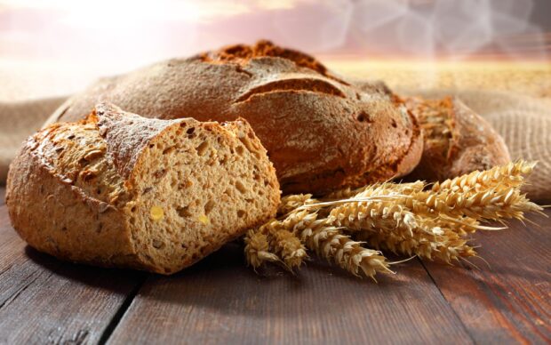 Freshly baked whole grain bread with wheat stalks on wooden table