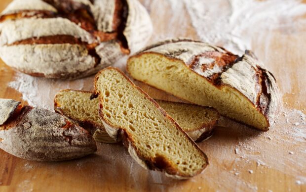 Rustic artisan bread with a soft texture on a wooden table with flour scattered around