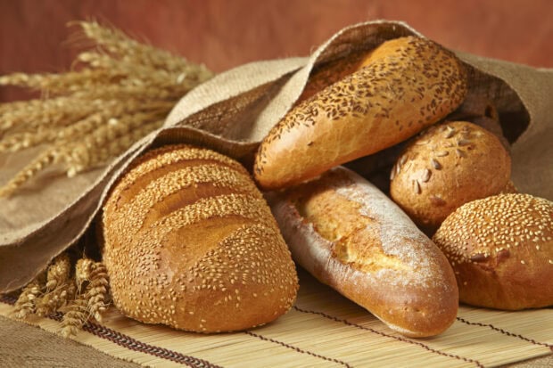 Freshly baked bread loaves with seeds arranged on a rustic mat and wheat stalks nearby