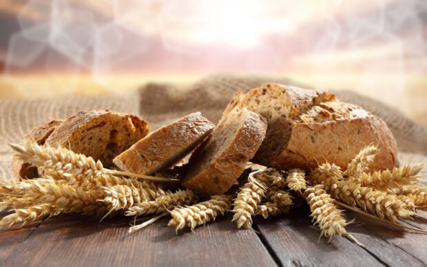 Freshly sliced bread with wheat stalks on a wooden surface under warm sunlight