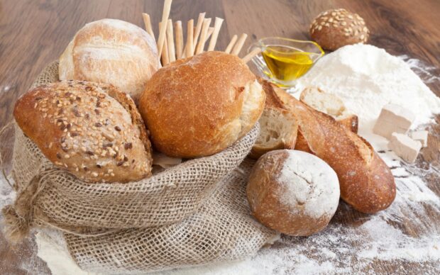 A variety of fresh bread loaves arranged on a rustic sackcloth with flour and olive oil on a wooden surface
