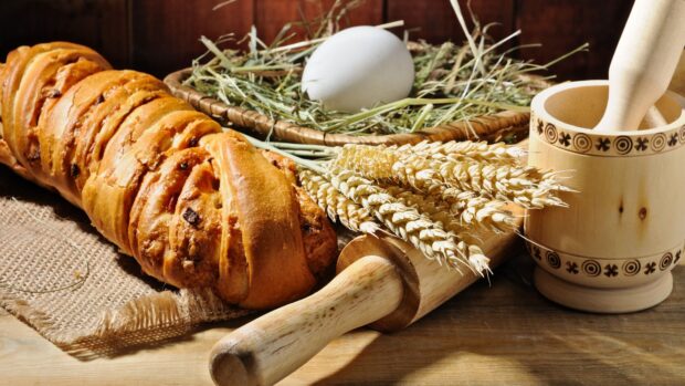 Fresh bread with wheat and an egg on a wooden table next to a rolling pin and mortar