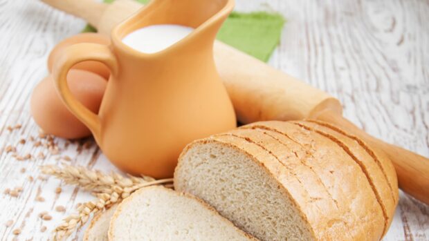 Fresh loaf of bread sliced on the table with wheat and milk pitcher