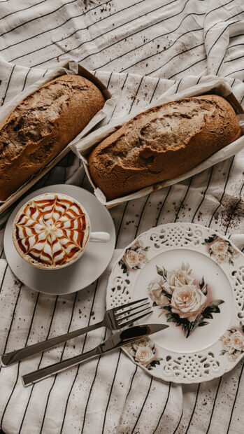 Two homemade bread loaves served with a decorated coffee on a striped tablecloth