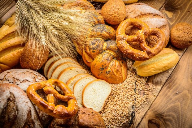 A variety of fresh bread with wheat grains on a wooden surface
